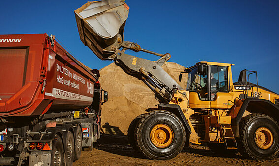 Ein Bagger belädt einen Kipplaster mit Sand und nutzt dabei die PFREUNDT Load & Go App